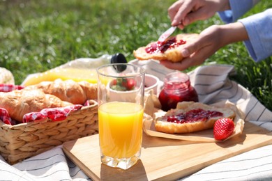 Woman with croissant outdoors, focus on glass of juice. Summer picnic