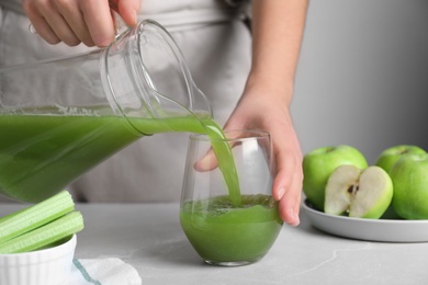 Photo of Woman pouring fresh celery juice in glass at light marble table, closeup