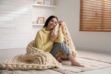 Young woman with chunky knit blanket on floor at home