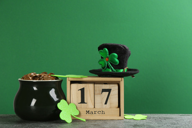 Composition pot of gold coins and wooden block calendar on grey stone table against green background. St. Patrick's Day celebration