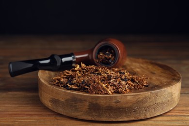 Board with smoking pipe and dry tobacco on wooden table against dark background