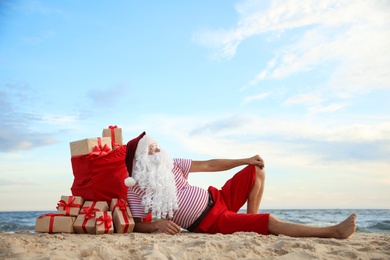 Santa Claus with bag of presents relaxing on beach, space for text. Christmas vacation