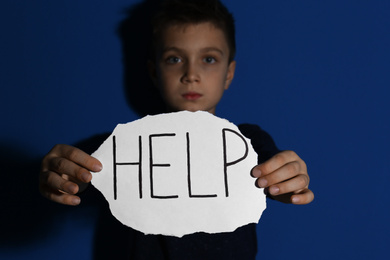 Photo of Abused little boy with sign HELP near blue wall, focus on hands. Domestic violence concept