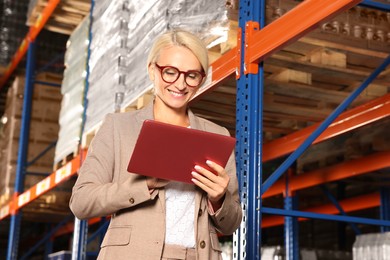 Happy manager using modern tablet in warehouse with lots of products