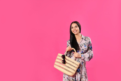 Young woman wearing floral print dress with straw bag on pink background. Space for text