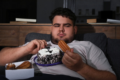 Depressed overweight man eating sweets in living room at night