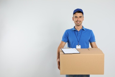 Happy young courier with cardboard box and clipboard on white background. Space for text