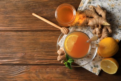 Cup of delicious ginger tea, honey and lemons on wooden table, flat lay. Space for text