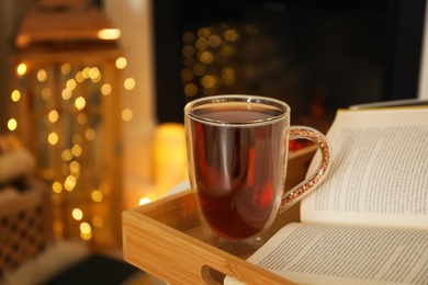 Cup of tea and book on wooden tray indoors