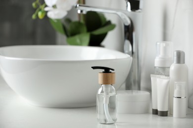 Bottle with dispenser cap and cosmetic products on white table in bathroom