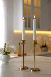 Photo of Pair of beautiful golden candlesticks on white marble table in kitchen