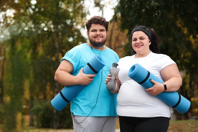 Overweight couple wearing sportswear with mats in park