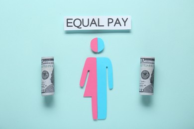 Photo of Equal pay concept. Human paper figure as male and female halves, dollar banknotes against light blue background, flat lay