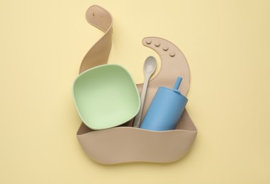 Photo of Baby feeding accessories and bib on yellow background, top view