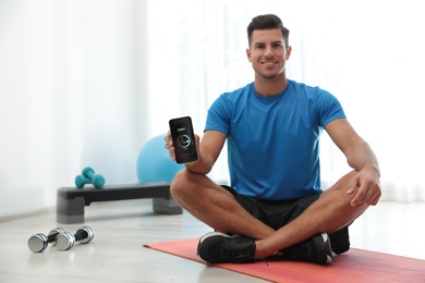 Man showing smartphone with fitness app indoors. Space for text