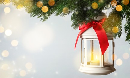 Christmas lantern with candle hanging on fir tree branch against light background, space for text 