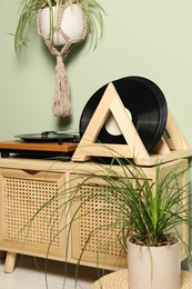 Vinyl records and player on wooden cabinet near light green wall