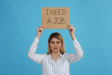 Photo of Unemployed woman holding sign with phrase I Need A job on light blue background