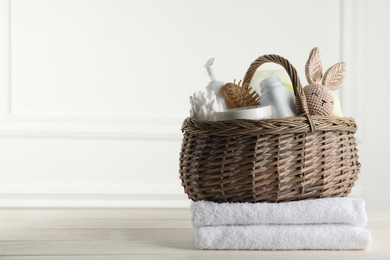 Wicker basket with different baby cosmetic products, accessories and toy on white wooden table. Space for text