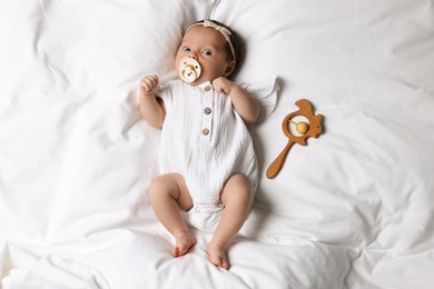 Cute little baby with pacifier and rattle lying on bed, top view