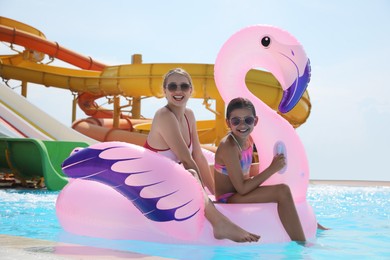 Mother and daughter with inflatable flamingo mattress in swimming pool at water park. Family vacation