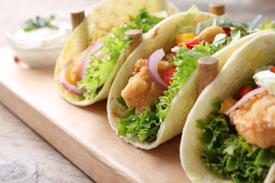 Photo of Yummy fish tacos on wooden table, closeup