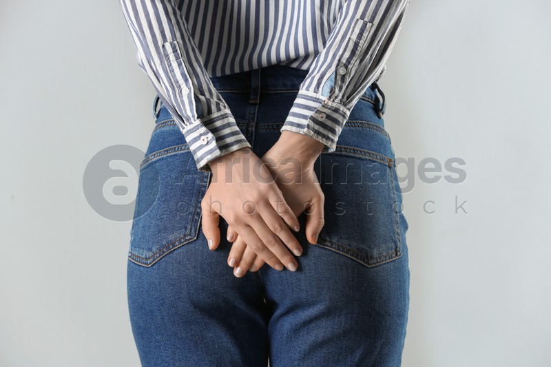Woman suffering from hemorrhoid on light grey background, closeup