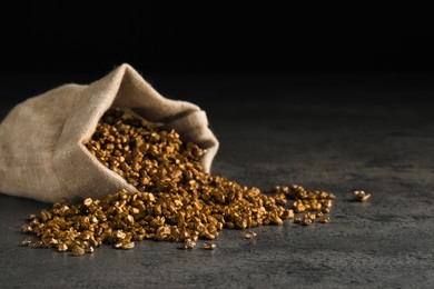 Overturned sack of gold nuggets on grey table against dark background, space for text