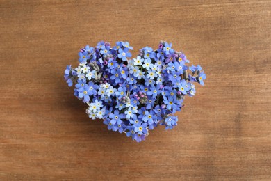Heart of beautiful blue forget-me-not flowers on wooden table, top view