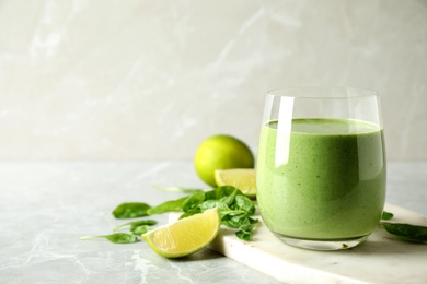 Glass of healthy green smoothie with fresh spinach on light table. Space for text