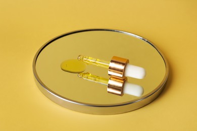 Photo of Dripping face serum from pipette on mirror against yellow background
