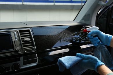 Man in gloves cleaning car dashboard with disinfectant spray and rag, closeup. Preventive measure during coronavirus pandemic