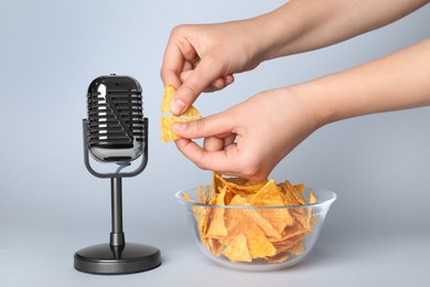Photo of Woman making ASMR sounds with microphone and nacho chip on grey background, closeup