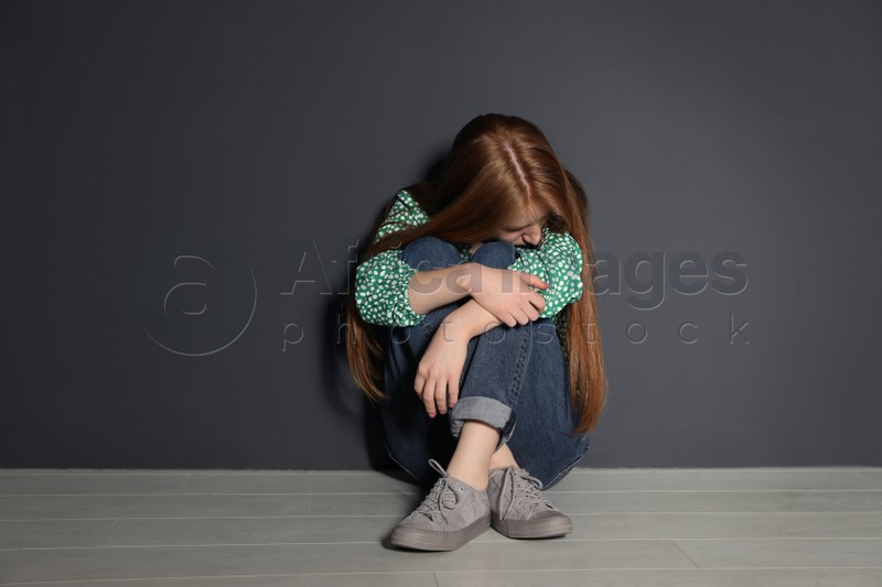Upset young woman sitting on floor near grey wall