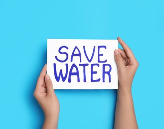 Photo of Woman holding card with words Save Water on light blue background, top view