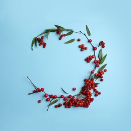 Red berries and leaves arranged in shape of wreath on light blue background, flat lay with space for text. Autumnal aesthetic