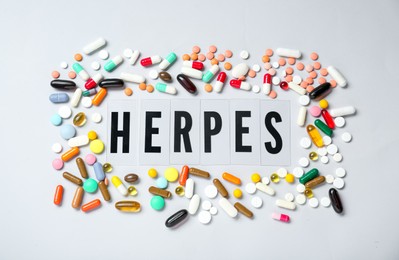 Word Herpes surrounded by different pills on white background, top view