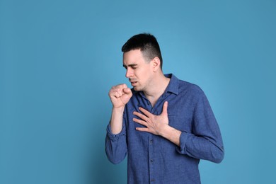 Young man coughing on blue background, space for text. Cold symptoms