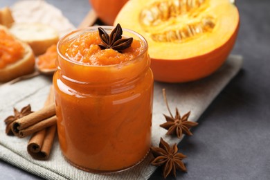 Jar of pumpkin jam, star anise, cinnamon and fresh pumpkin on grey table, closeup