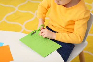 Photo of Boy cutting green paper at desk in room, closeup. Home workplace
