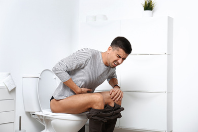 Man with stomach ache sitting on toilet bowl in bathroom
