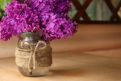 Beautiful lilac flowers in glass jar on wooden table indoors. Space for text