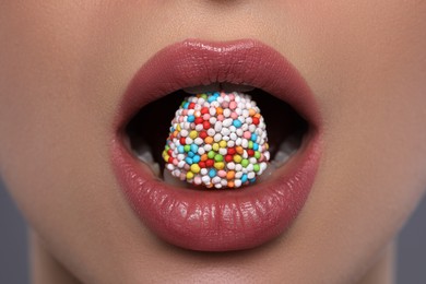 Woman with beautiful lips eating candy on grey background, closeup