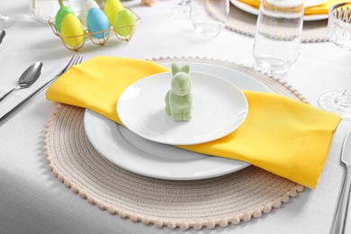Photo of Festive table setting with cutlery, plate and bunny figure. Easter celebration