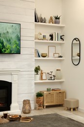 Shelves with different decor near decorative fireplace in living room. Cozy interior design