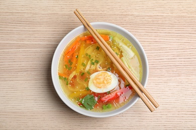 Bowl of tasty ramen with noodles, vegetables and chopsticks on wooden table, top view