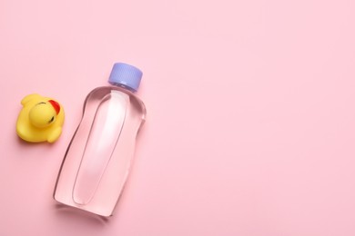 Photo of Bottle of baby oil and toy duck on pink background, flat lay. Space for text