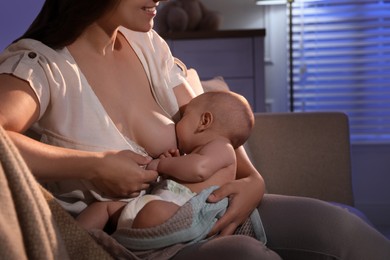 Young woman breastfeeding her little baby indoors at night, closeup