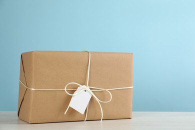 Parcel wrapped in kraft paper with tag on white wooden table against light blue background