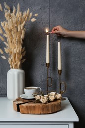 Woman lighting candle on table near grey wall indoors, closeup. Interior design